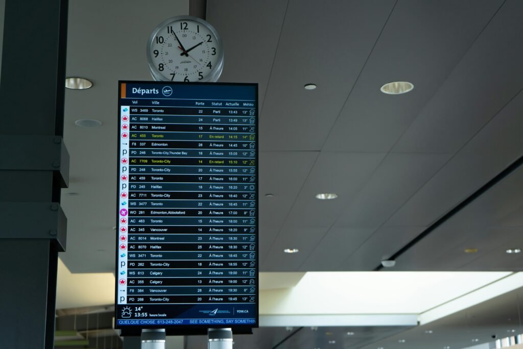 Airport departure screen showing various flight schedules and times with a wall clock above.